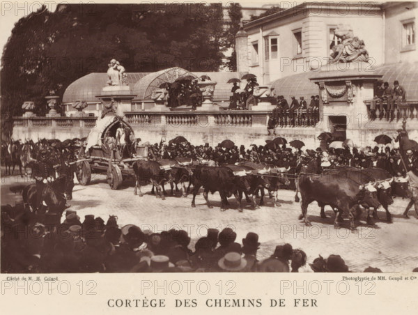 Nervian ox cart, at a parade for the railways in Brussels, Cortège des chemins de fer, chariot Nervien (Bruxelles 1885), page, photomechanical print, photographer: Hector Colard, Brussels, cliché maker: Goupil & Cie., Paris, 1885, printer (person), paper, Woodburytype, height 103 mm x width 161 mm, Print on unnumbered page., public festivities, four-wheeled vehicle drawn by more than three animals, festivities, corporative organization, guild, A wide street scene shows a procession with a team of oxen pulling a wooden wagon that has a curved canopy and figures standing on and around it, a large crowd lines the route with many people holding umbrellas and wearing hats, a stone balustrade and terrace above the street is occupied by seated and standing spectators, a building with classical ornamentation and sculptural figures sits behind the terrace, decorative stone urns and carved details adorn the balustrade, several mounted riders are visible among the crowd, and trees rise behind the...