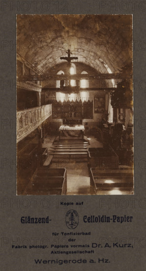 Interior of St. John's Church in Wernigerode, photograph, page, photographer: Hermann Günther, Wernigerode, 1923 - 1928, Hermann Günther, photographer, Saxony-Anhalt, paper, baryta paper, daylight collodion silver print, height 135 mm x width 88 mm, interior of church, St. John's Church, A sepia-toned interior photograph shows a vaulted stone ceiling with visible masonry and arched windows at the far end, through which bright light filters into the space. A large crucifix hangs from a horizontal beam near the ceiling, silhouetted against the light. Below, an altar covered with a draped cloth stands in front of an ornate altarpiece composed of framed panels and decorative pinnacles. Wooden pews and benches are arranged in rows leading toward the altar, and carved wooden galleries or paneling run along the left wall. Decorative elements, framed pictures, and sculptural details appear along the side walls, and a pulpit or carved wooden structure is visible on the right. The photograph is ...