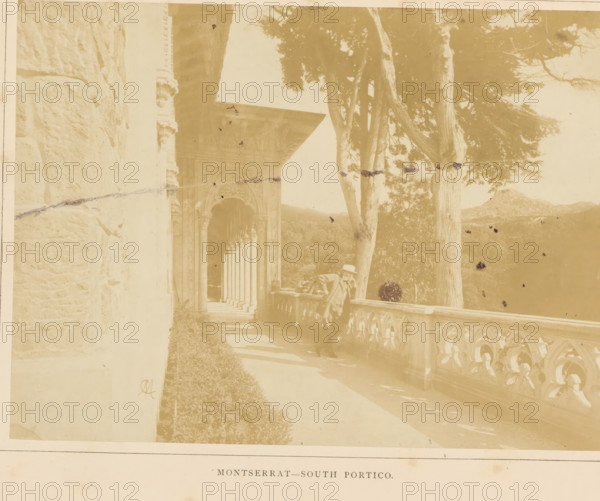 South portico of the Palácio de Monserrate near Sintra, Montserrat - South Portico, photograph, page, monogram: 'M', Sintra, c. 1865 - in or before 1870, photographer, paper, albumen print, albumendruk, height 146 mm x width 199 mm, colonnade, palace, gate, entrance, Palácio de Monserrate, A sepia-toned photograph showing an ornate stone portico with a row of carved columns and arches receding into the background beside a balustraded terrace, a man wearing a hat leaning on the terrace railing, tall trees with textured trunks rising beside the terrace, a stone wall at the left edge, decorative architectural details around the archway, shadows cast on the walkway, and distant hills visible beyond the trees.
