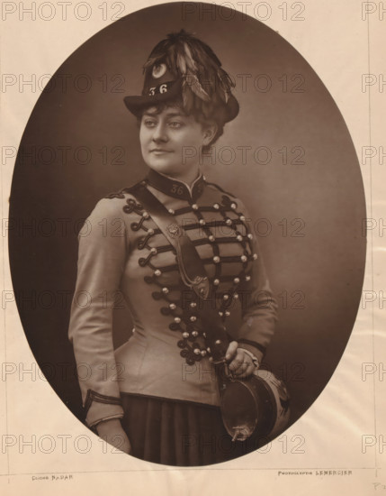 Portrait of Grisier-Montbazon, page, photomechanical print, photographer: Félix Nadar, cliché maker: Lemercier, c. 1880 - c. 1885, paper, Woodburytype, Woodburytypie, height 264 mm x width 204 mm, Person, Marie Grisier-Montbazon, historical persons - BB - woman, portrait of actor, actress, A sepia portrait of a woman shown from the waist up inside an oval frame, wearing a decorated military-style jacket with braided cords and shiny buttons, a sash across her chest with an ornamental badge, a pleated skirt, and a hat adorned with long feathers; she holds a round drum by its strap in one hand and looks slightly to the side with a neutral expression.
