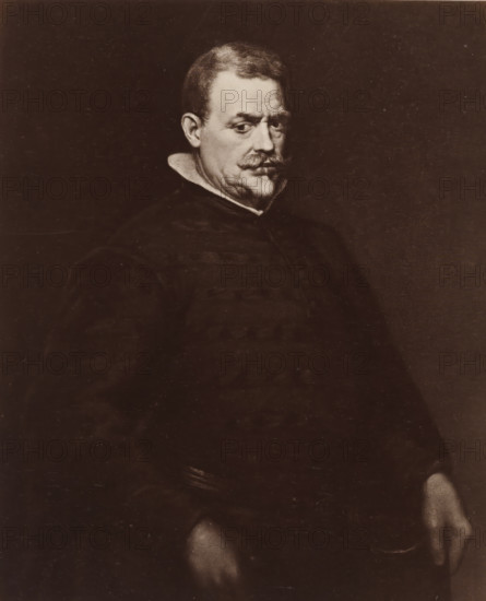 Photo reproduction of a painted portrait of Don Juan Mateos by Diego Velázquez, D. Velasquez: Männliches Bildniss, photograph, reproduction, page, after painting by Diego Rodriguez de Silva y Velázquez, publisher: Photographische Gesellschaft Berlin, Berlin, c. 1870 - in or before 1875, photographer, paper, albumen print, height 211 mm x width 175 mm, Photo on unnumbered page., Person, Juan Mateos, historical persons, A sepia-toned portrait of a man seated against a dark background, showing his head and upper body turned slightly to one side, with short hair and a prominent mustache, a high white collar visible at his neck, dark clothing with broad shoulders, and hands resting at his sides, one hand partially visible at the lower edge of the image.