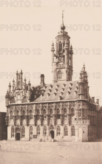 View of the Town Hall of Middelburg, photomechanical print, c. 1850 - c. 1900, paper, collotype, photogravure, height 261 mm x width 188 mm, town hall, Middelburg, Stadhuis (Middelburg), A sepia-toned photograph of an ornate Gothic-style building with a large central tower rising above a steeply pitched roof dotted with small dormer windows, the tower featuring arched openings, decorative columns, a round clock face, and a bulbous spire topped by a finial; the facade below displays tall arched windows with tracery, sculpted figures in niches, pinnacles, and decorative stonework, while the ground level shows arched doorways with patterned shutters and a small raised platform or entrance feature with steps in front; the foreground is a cobbled open area.