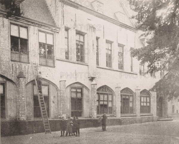 View of the former residence of the abbot in the inner courtyard of the Abbey in Middelburg, 1894, Former residence of the abbot, later of the bishop, Ancien logement de l'abbé, Views of the Abbey in Middelburg, Abbey in Middelburg, Abbaye de Middelbourg, photomechanical print, cliché maker: Straaten, Gebroeders van, Middelburg, in or after 1900, Straaten, photographer, cliché maker, paper, collotype, photogravure, height 149 mm x width 185 mm, courtyard, abbey, monastery, convent, Roman Catholic church, Abbey of Middelburg, A faded façade of a multi-storey building with tall rectangular windows set above a row of arched openings, rough stone walls and visible mortar, and decorative ironwork on some window ledges; a long ladder leaning against the wall reaching toward an upper window where a person stands partway up; a small group of children standing together in the courtyard in front of the building and another person standing nearby facing toward them; a tree with dense foliage part...