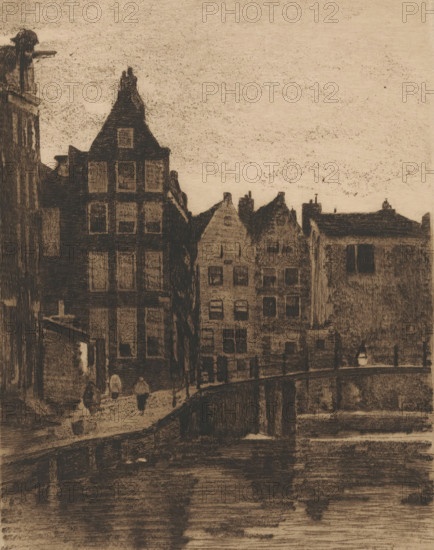 View of houses and a bridge in Amsterdam, print, printmaker: Willem Witsen, Amsterdam, c. 1915 - c. 1919, paper, etching, intaglio printmaking technique, aquatint, soft-ground etching, plate tone and soft-ground varnish, height 236 mm x width 186 mm, urban housing, canals, waters (in city), bridge, A sepia-toned scene of tall, narrow buildings with steep gabled roofs clustered along a canal, their dark facades and window openings rendered with dense crosshatching, a curved stone bridge crossing the water in the foreground, a few small silhouetted figures walking near the buildings, a single lamp post on the bridge, and faint reflections of the architecture visible on the water's surface under a textured, empty sky.