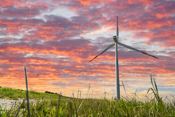 Bavaria, Germany - 11 February 2025: PHOTOMONTAGE, wind turbine on a green meadow in front of a colorful sunset symboliz