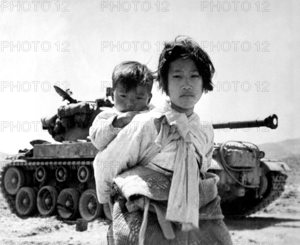 Korea: With her brother on her back a war-weary Korean girl trudges by a M-26 tank at Haengju. Korean War (1950-1953). T
