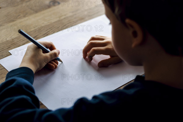 Symbolfoto zum Thema Linkshaender: Ein fuenfjaehriger Junge sitzt zu Hause und schreibt mit einem Bleistift in der linke