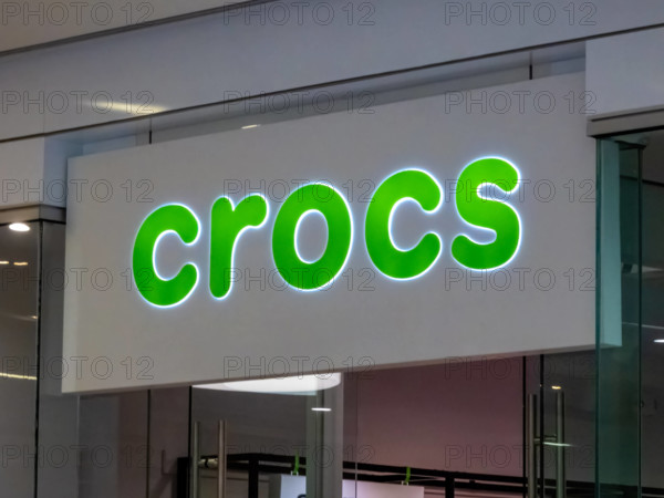 Edmonton, Alberta, Kanada. 24. Mai 2025. Das markante, grün beleuchtete Crocs-Logoschild signalisiert die Präsenz der beliebten Schuhmarke und zieht mit seinem verspielten Design die Aufmerksamkeit auf sich.