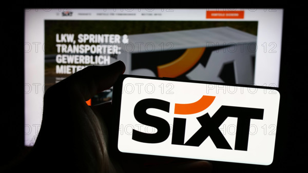 Person holding smartphone with logo of German car rental company Sixt SE in front of website. Stuttgart, Germany - 08-06