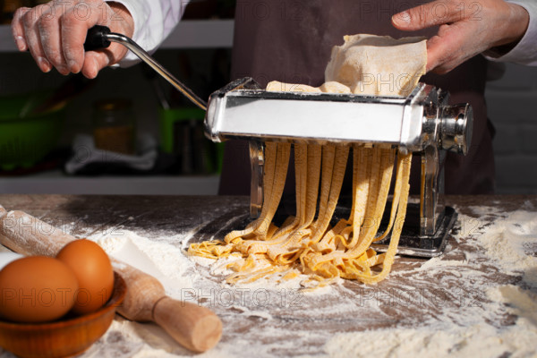 Kaukasische weibliche Hände bei der Herstellung von Fettuccine-Nudeln mit einer mechanischen Nudelmaschine