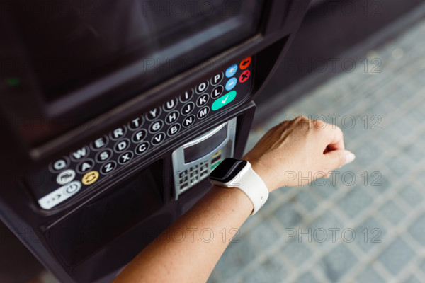 Person, die mit einer Smartwatch kontaktlos bezahlt, um einen Parkplatz zu bezahlen. Bezahlen am Parkautomaten. Ein Kunde bezahlt sein Parkticket schnell und einfach kontaktlos mit einer Smartwatch. Verwendung der NFC-Technologie
