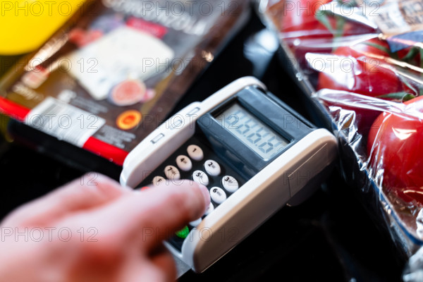 Bavaria, Germany - August 27, 2025: A customer enters their PIN on the card reader at the supermarket checkout. Illustra