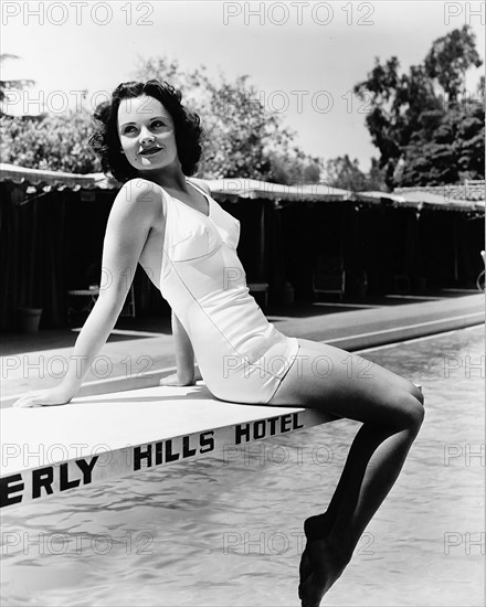 L'actrice Elizabeth Earl assise sur le plongeoir d'une piscine au Beverly Hills Hotel
