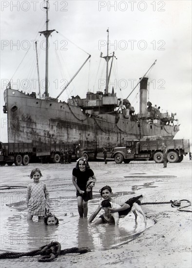 Fillettes jouant sur une plage d'Arromanches, devant un bateau allié