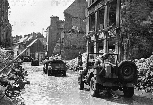 American troops in jeeps making their way through a bomb damaged Normandy town in Northern France shortly after the D-Day landings begun the Allied invasion of the continent during World War Two July 1944.