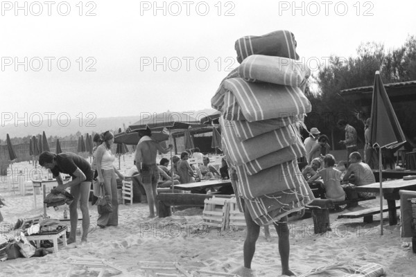 Saint-Tropez, France, 17th June 1975, man carrying Sun Lounger Cushions.