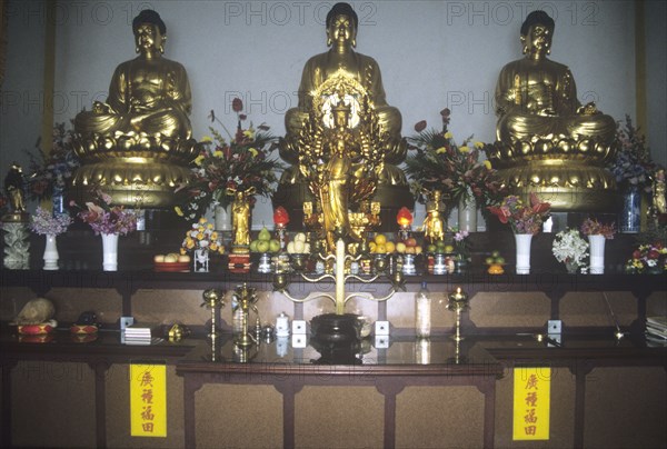 Chinese temple altar with row of Buddhas and kannon (female) with offerings
