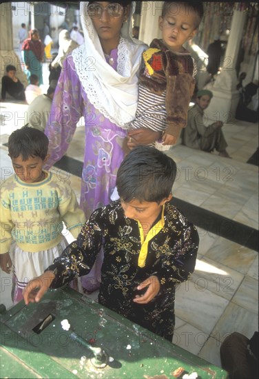 Mother teaching her son the meaning of giving in a mosque in Lahore