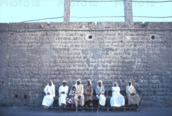 Arab men and a girl sitting on a street bench in Ajman during the fast month of Ramadan