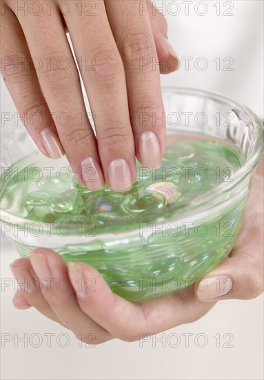 Female fingers in a dish of aloe gel.