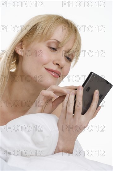 Woman using PDA in bed.