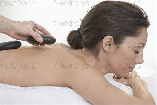 Masseuse placing stone on woman's back.