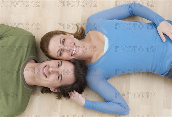 Smiling couple lying on wood floor.