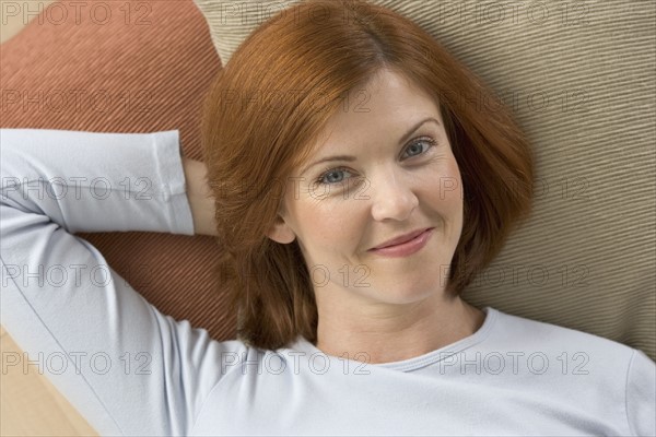 Smiling redheaded woman lying on pillows.