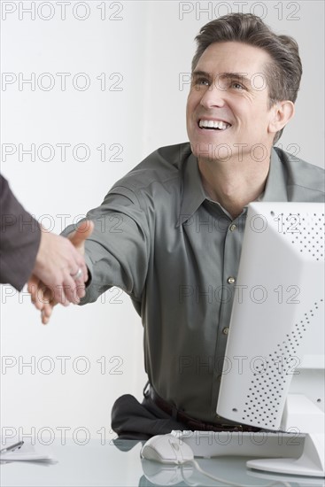 Businessman at desk shaking hands.