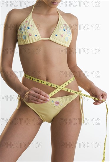 Woman in bikini measuring her waist.