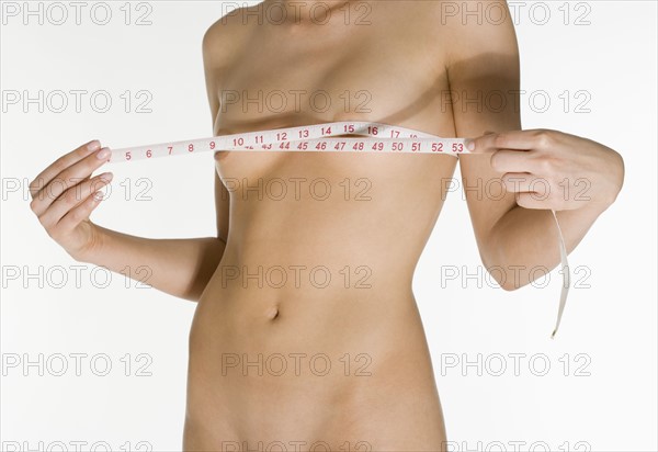 Nude female measuring her breasts.