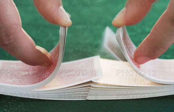 Hands shuffling cards on poker table.