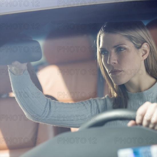 Woman in car adjusting rearview mirror.