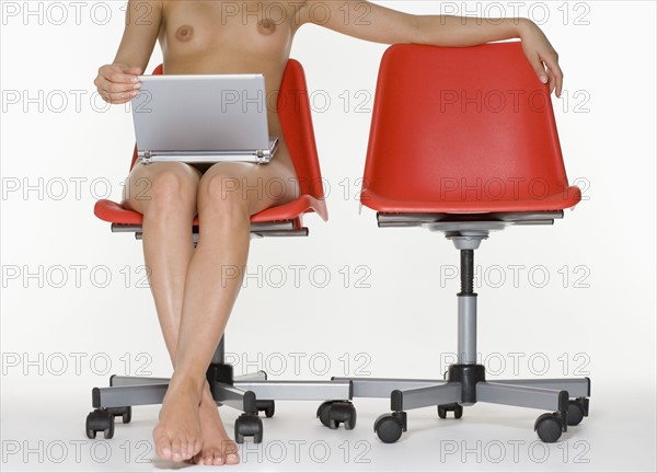 Nude female sitting with laptop computer.