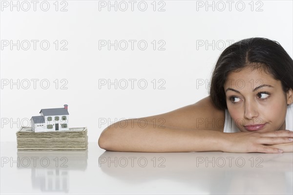 Woman looking at miniature house and money.