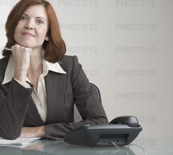 Attractive businesswoman with phone at desk.