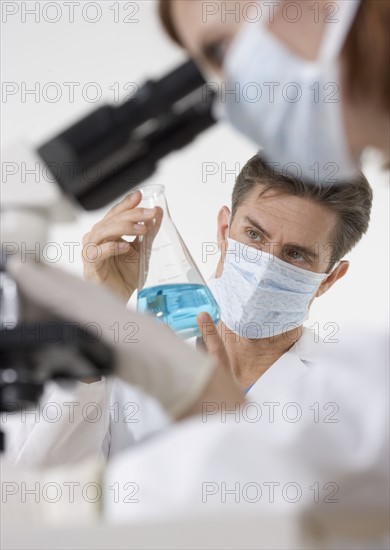 Scientists with microscope and blue liquid.