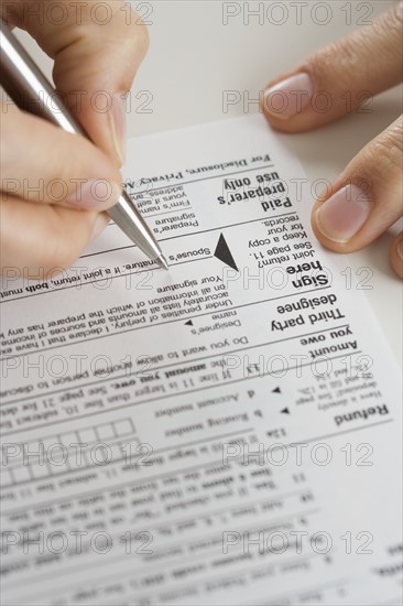 Closeup of hands signing tax form.