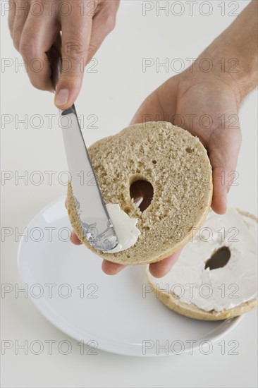 Hand spreading cream cheese on bagel.