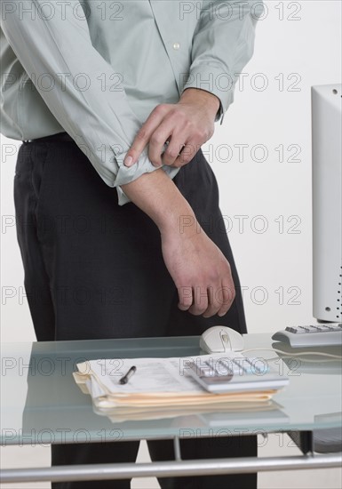 Man at desk rolling up his shirt sleeves.