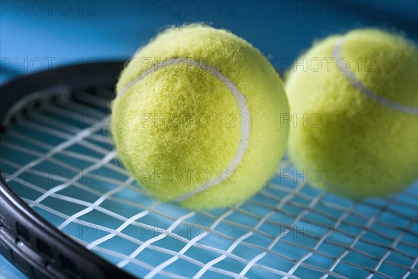 Closeup of tennis racquet and two balls.