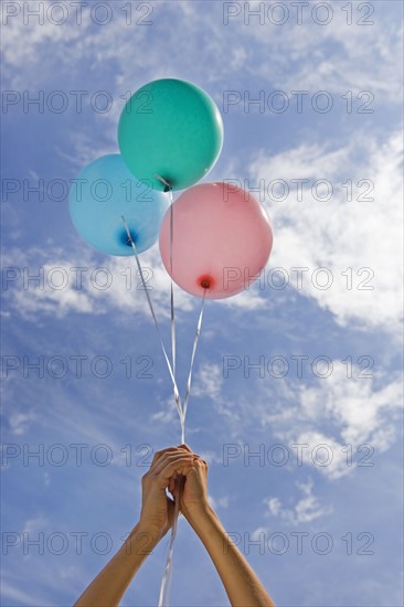 Hands holding balloons toward sky.