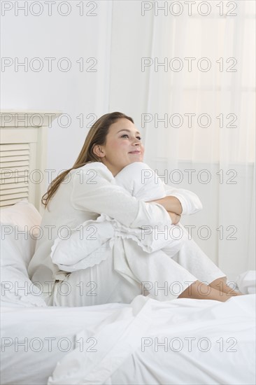 Woman on bed hugging her knees.