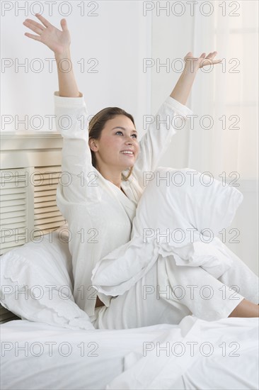 Woman sitting on bed with her arms raised.
