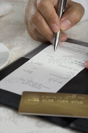 Close up of man signing credit card receipt at restaurant.