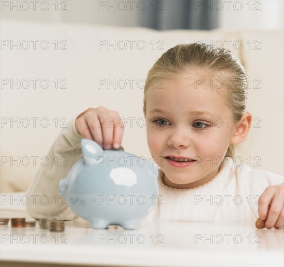 Young girl putting change in piggy bank.