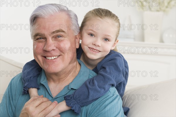 Grandfather and young granddaughter hugging on sofa.