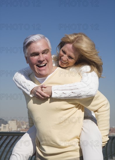Senior man giving senior woman piggy back ride outdoors.