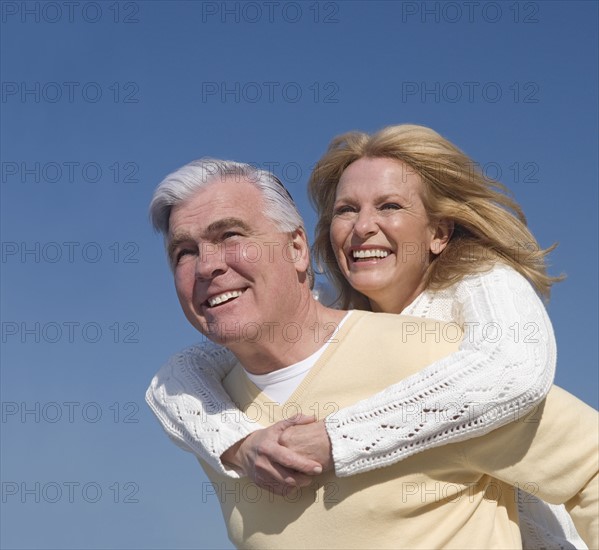 Senior man giving senior woman piggy back ride outdoors.