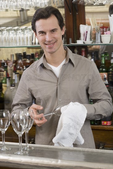 Male bartender drying wine glasses.